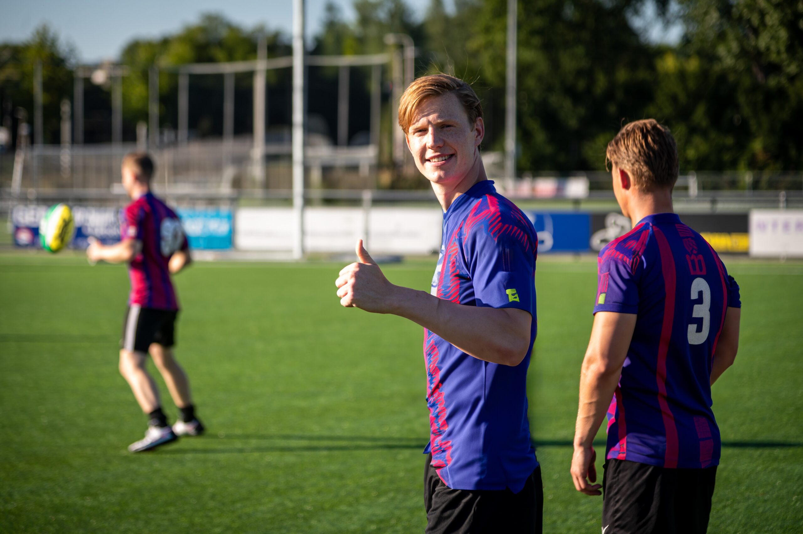 Afbeelding waarin drie mannen te zien zijn die rugby spelen